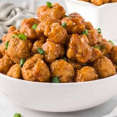 a white bowl filled with meatballs covered in sauce and garnished with green onions