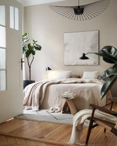 a bedroom with a bed, chair and potted plant on the floor in front of it