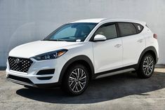 a white car is parked in front of a gray wall and cement floored parking lot