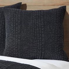 two black pillows sitting on top of a bed next to a wooden headboard and night stand