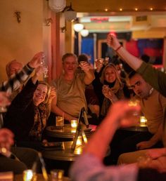 a group of people sitting at a table with wine glasses in their hands and smiling