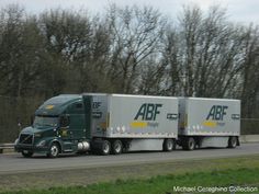 a semi truck driving down the road with trees in the background