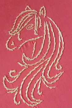 an embroidered horse head on a pink background with white thread in the shape of a woman's face