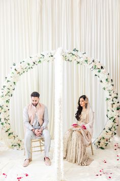 a man and woman sitting in front of a white arch