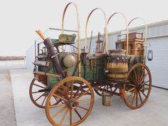 an old - fashioned wagon is parked in front of a building with several barrels on it