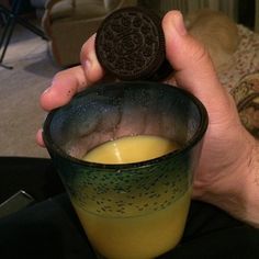 a man holding up a glass with an oreo cookie in it's hand