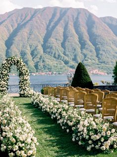 rows of chairs with white flowers in front of the mountains and water are set up for an outdoor ceremony