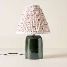 a green table lamp sitting on top of a white counter next to a light bulb