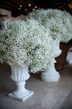 three white vases filled with baby's breath flowers on top of a tiled floor