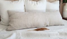 a white bed topped with lots of pillows next to a vase filled with pink flowers