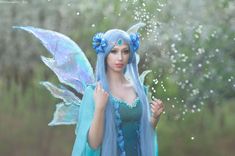 a woman dressed as a fairy with blue hair and wings standing in front of water