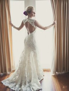 a woman standing in front of a window with her back turned to the camera and wearing a wedding dress