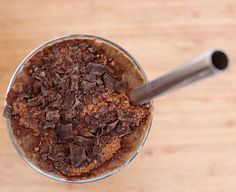 a chocolate dessert in a glass on top of a wooden table with a metal straw