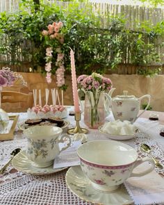 a table topped with cups and saucers filled with cake next to a vase full of flowers