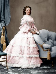 an old fashion photo of a woman in a pink dress standing next to a chair