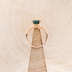 a gold ring with a green stone on it sitting on top of a piece of wood