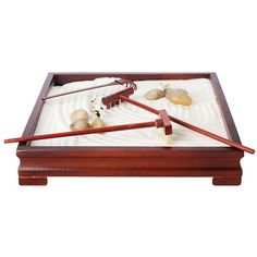 a wooden tray with rocks and chopsticks in it on top of sand covered ground