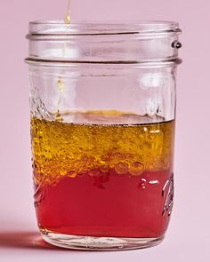 a glass jar filled with liquid on top of a pink table next to a white wall