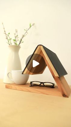 a wooden stand with a cup and eyeglasses on it next to a vase