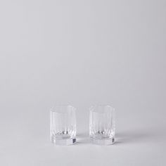 two clear glasses sitting side by side on a white surface with one glass half empty