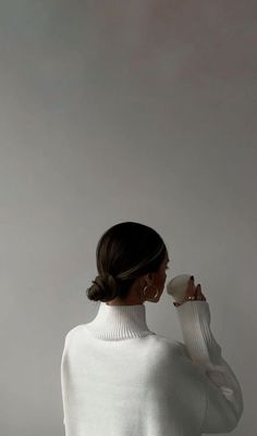 a woman in white sweater drinking from a cup