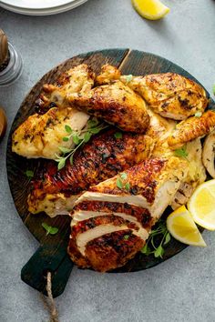 grilled chicken with lemons and herbs on a wooden platter next to other food