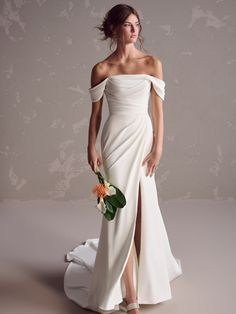 a woman in a white dress is holding a flower and posing for the camera with her hand on her hip