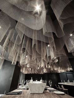 a wooden table topped with plates and glasses under a ceiling covered in gold mesh netting