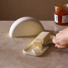 a person cutting cheese with a knife on a counter next to a jar of jam