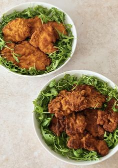 two white bowls filled with fried chicken and green lettuce on top of a table