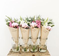 four vases with flowers in them sitting on a wooden table next to each other