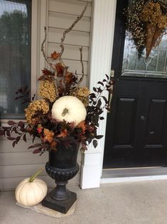 a black vase with white pumpkins and flowers on the front porch next to a door