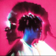 a man with dreadlocks standing in front of a pink background