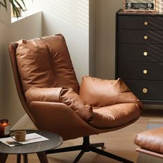 a brown leather chair and ottoman in a living room with a black chest of drawers