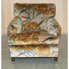 an upholstered chair sitting in front of a wooden paneled wall with birds on it