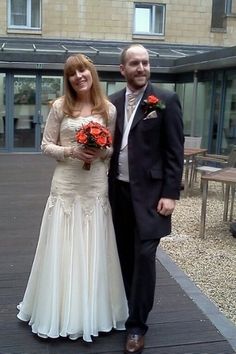 a man and woman in formal wear posing for the camera on a wooden deck outside an apartment building