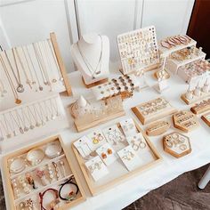 a table topped with lots of jewelry on top of a white table covered in wooden trays