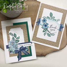 two cards with flowers on them sitting next to a potted plant and a wooden slice