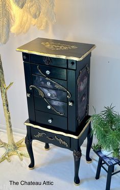 a black and gold painted chest of drawers next to a small stool with a potted plant on it