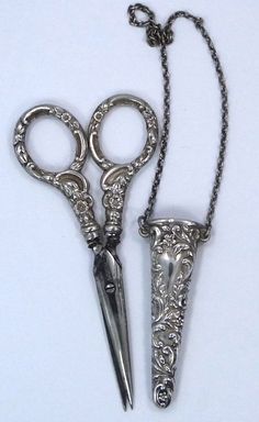 two pairs of scissors are attached to a chain on a white surface with an ornate design