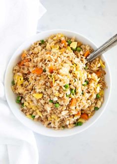 a bowl filled with rice and vegetables on top of a white table cloth next to a spoon