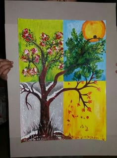 a person holding up a piece of art with four different trees painted on the sides