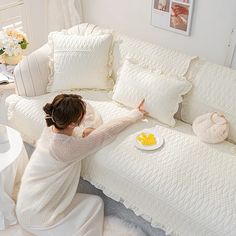 a woman sitting on a couch in front of a white sofa with pillows and plates