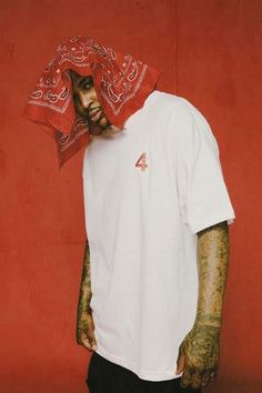 a man with tattoos and a bandana on his head standing in front of a red wall