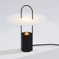 a black table lamp with a white shade on top and a round light in the middle