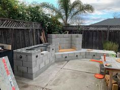 an outdoor kitchen made out of cinder blocks in the middle of a backyard with tables and chairs around it