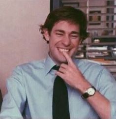 a man wearing a blue shirt and black tie smiles at the camera while sitting in an office