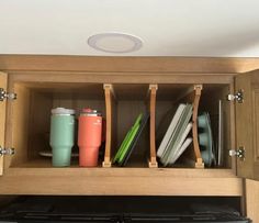 an open cabinet with coffee cups and other items in the bottom shelf, on top of a stove