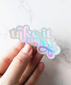 someone holding up a sticker with the words take it easy in rainbow letters on it