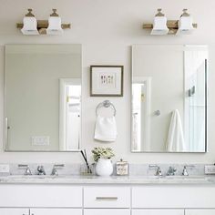 a white bathroom with two sinks and three mirrors on the wall above them is shown